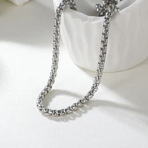 Polished silver stainless steel 2mm box chain necklace draped on white ceramic vessel