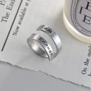Detail of 'I am Enough' engraved ring on aesthetic newspaper and candle background