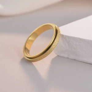 Detail of 4mm golden rotating stress relief ring with frosted finish on stone background