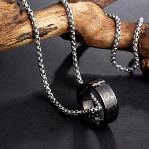 Close-up of a fishhook pendant with a black ring on a silver chain over driftwood