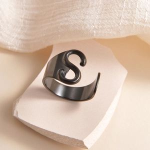 Detalle macro de un anillo negro con letra S sobre un soporte de piedra minimalista