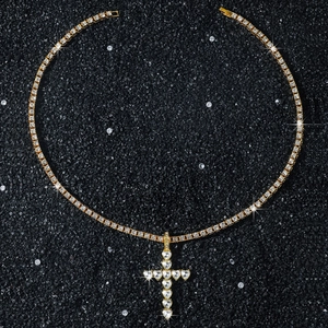 Macro d'une chaîne tennis dorée avec pendentif croix en cristaux cœur sur sable noir