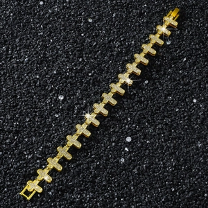 Détail d'un bracelet hip hop doré avec maillons croix et cristaux sur fond de pierres noires