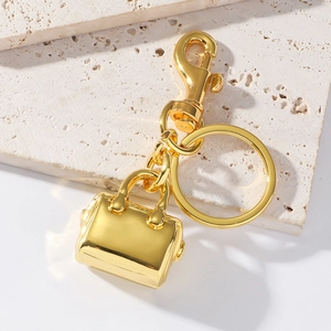 Porte-clés sac à main doré avec mousqueton posé sur un support en travertin beige
