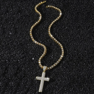Gold hip hop cross pendant with paved zircons on a tennis chain over black sand texture