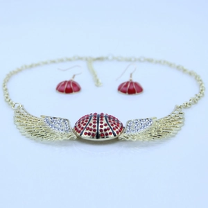 Dettaglio macro della collana con ali dorate e orecchini in cristallo rosso