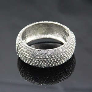 Bracelet jonc large argenté orné de strass blancs étincelants sur un fond noir réfléchissant