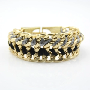 Detail of chunky gold alloy Cuban link bracelet with interwoven black textile cords