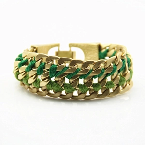 Close-up of matte gold chunky woven bracelet with green thread details and square buckle
