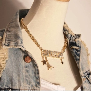 Detail of chunky gold chain necklace with SUPERSTAR rhinestone pendant on denim vest