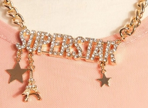 Detail of gold-tone Cuban chain necklace with rhinestone SUPERSTAR letters and charms