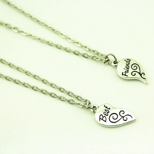 Détail de deux pendentifs cœur brisé argentés avec gravure Best Friends et volutes