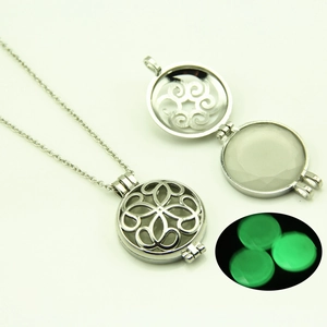 Détails d'un collier médaillon argenté ajouré avec une perle lumineuse verte à l'intérieur