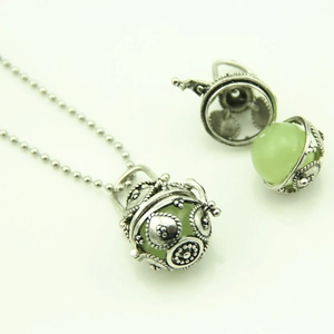 Détail d'un pendentif sphère évidée vintage avec perle lumineuse verte et chaîne argentée