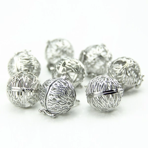 Close-up of hollow silver locket charms with intricate filigree texture on white background