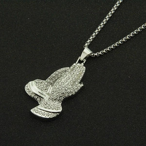 Gros plan du pendentif mains de prière argenté avec chaîne box sur fond noir texturé