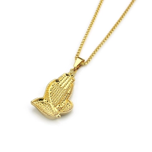 Macro detail of golden praying hands pendant with textured grain finish and mesh chain