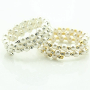 Detailed view of multilayer spiral bracelets with rhinestones and white pearls in silver and gold