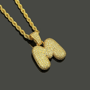 Close-up of golden bubble letter M pendant with paved zircons on a gold rope chain