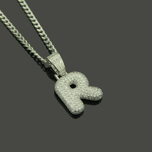 Close-up of silver letter R pendant with micro-pave zircons on a cuban chain link