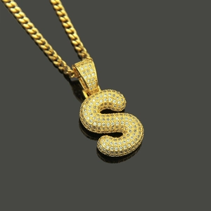 Macro detail of iced-out gold letter S pendant on a thick cuban link chain