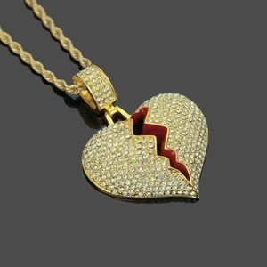 Détail du pendentif cœur brisé doré serti de strass avec émail rouge sur une chaîne torsadée