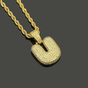 Macro view of iced out letter U pendant with white zircons on a gold rope chain