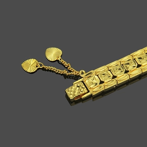 Gold watch-style bracelet with rhombic patterns and a heart charm on a black surface
