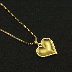 Close-up of golden heart pendant with matte finish and wavy borders on black surface