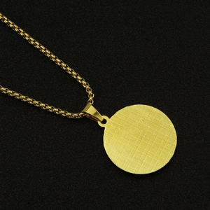 Vue détaillée du pendentif rond doré à texture quadrillée sur une chaîne vénitienne
