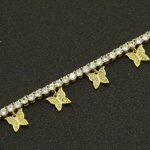 Close-up of golden tennis chain necklace featuring pave zircon butterfly charms on black background