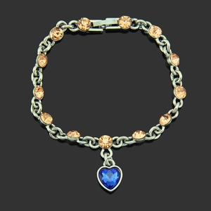 Elegante bracciale con cristalli champagne e ciondolo a cuore blu su sfondo nero