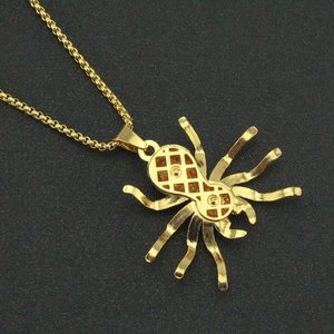 Close-up of golden spider pendant with red stone inlay and intricate mesh design