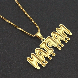Macro detail of gold WATFAM letter pendant in street style with bead chain on dark surface