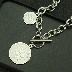 Détail d'une chaîne argentée à fermoir OT avec pendentif pièce et breloque Love