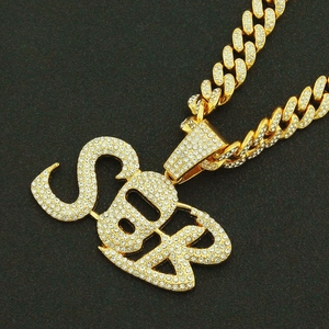 Macro detail of iced out SBR alphabet pendant on a golden cuban link hip hop necklace