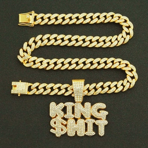 Macro detail of gold hip hop pendant with KING $HIT letters and iced out cuban link chain