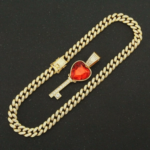Détail du collier chaîne cubaine dorée avec pendentif clé en cœur et pierre rouge rubis
