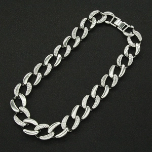 Détail du collier chaîne cubaine argentée avec strass scintillants sur fond noir mat