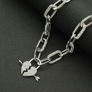 Silver Cuban link necklace with iced out heart and arrow pendant on a black surface