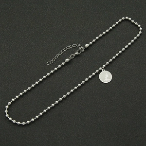Macro detail of silver bead chain necklace with vintage 1990 coin pendant on black surface