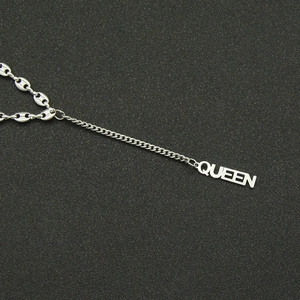 Detail of silver pig nose chain with QUEEN letter pendant on black textured surface