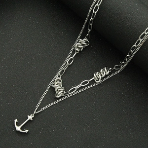 Silver layered necklace featuring anchor pendant and textured knot on cuban chain