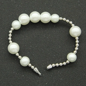 Détail de perles blanches alternées et de cylindres métalliques argentés sur bracelet