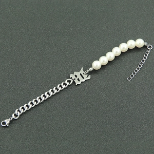 Detail of silver Cuban chain bracelet with letter B charm and white pearls on dark surface