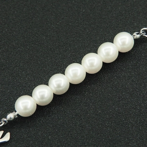 Macro detail of glossy white pearls and silver metal chain links on a black background