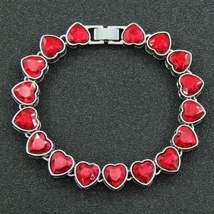 Dettaglio di bracciale con cristalli a cuore rosso e maglie argentate su fondo nero