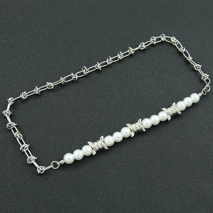 Barbed wire style stainless steel necklace with elegant white pearls on a dark surface