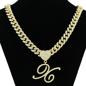Detailed view of iced out golden Cuban link chain with a sparkling script letter X pendant