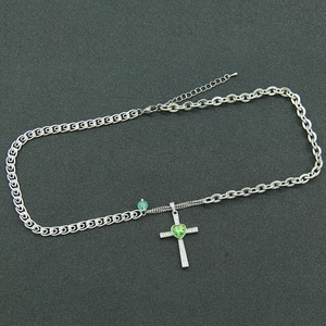 Cross necklace with green heart gem and mixed chain links on a textured background